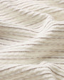 Close-up image of cream-colored fabric with a soft, ribbed texture, featuring fine horizontal lines in subtle tonal variation. The material is gently folded to highlight the drape, depth, and plush surface of the textile.