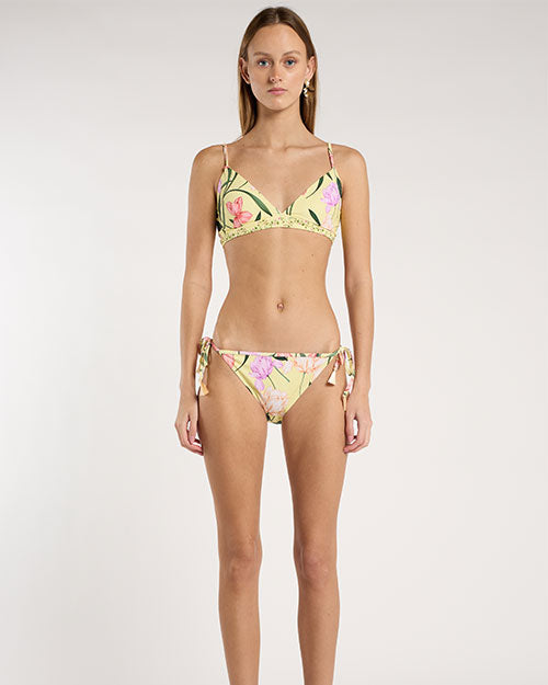 Person standing against a neutral backdrop, wearing a yellow floral bikini. 
