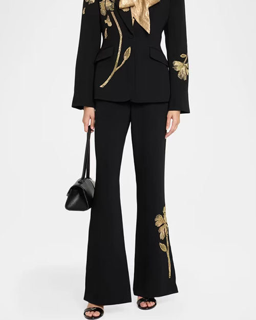 Black tailored suit with gold floral embroidery on the blazer and flared pants, paired with a gold neck scarf, black handbag, and open-toe heels.