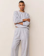 Person wearing a matching light gray loungewear set with a subtle embossed pattern, consisting of a long-sleeve sweatshirt and relaxed-fit pants, standing against a plain beige background with arms crossed.