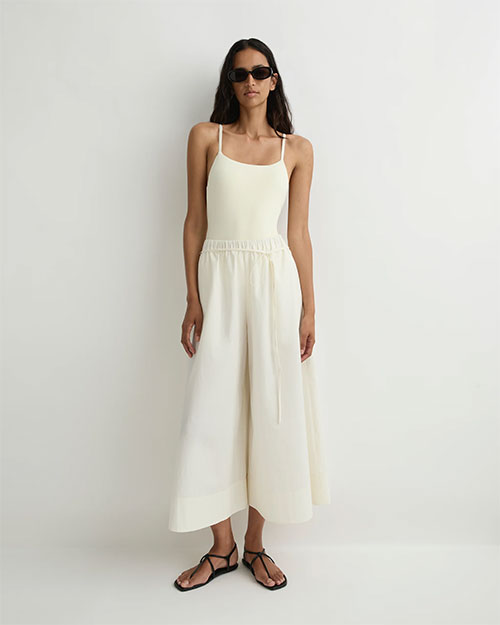 Person modeling a sleeveless cream camisole with thin straps and matching wide-leg pants featuring a drawstring waist, paired with black flat sandals and sunglasses against a plain light background.