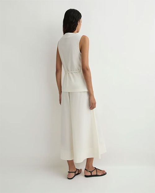 Rear view of a person modeling an ivory sleeveless wrap-style top with a side tie and matching wide-leg cropped pants against a plain light background.