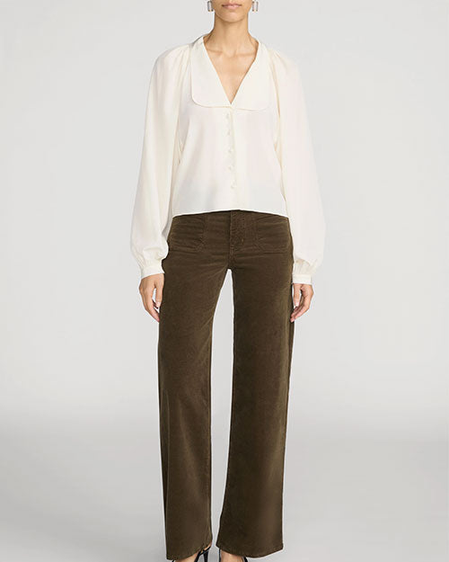 Front view of a person wearing a cream-colored blouse with a deep V-neckline, covered buttons, and long billowy sleeves gathered at the cuffs. The blouse is paired with high-waisted brown wide-leg corduroy pants featuring a straight, relaxed fit. The outfit is shown against a light gray background, with dark pointed-toe shoes partially visible at the hem.