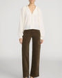 Front view of a person wearing a cream-colored blouse with a deep V-neckline, covered buttons, and long billowy sleeves gathered at the cuffs. The blouse is paired with high-waisted brown wide-leg corduroy pants featuring a straight, relaxed fit. The outfit is shown against a light gray background, with dark pointed-toe shoes partially visible at the hem.