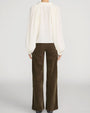 Back view of a person wearing a cream-colored blouse with a loose, flowing silhouette and long voluminous sleeves gathered at the cuffs. The blouse falls to the hips and features soft pleating across the upper back. It is paired with high-waisted brown wide-leg corduroy pants with a straight-leg fit and subtle back pocket detailing. Dark pointed-toe shoes are partially visible below the hems. The outfit is shown against a light gray background.