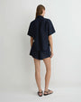 Back view of a person wearing a dark navy short-sleeve button-up shirt with matching shorts, black flat sandals against a plain white background.