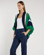 Person standing in a studio against a light neutral background, wearing a white scoop-neck tank top layered under a cropped, open-front cardigan with textured color‑block stripes in green, navy, light blue, and cream.