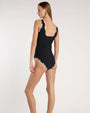 Person wearing a black, scoop neck, one piece swimsuit with beige and blue geometric piping. 