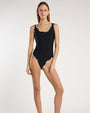 Person wearing a black, scoop neck, one piece swimsuit with beige and blue geometric piping. 