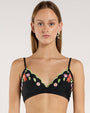 Image of a person's torso, wearing a scalloped black bikini top embroidered with green leaves and pink and purple flowers. 