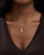 Close-up of a neck wearing two gold necklaces. One has a hollow heart-shaped pendant, and the other features a cylindrical charm with intricate detailing.