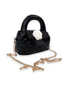 Small black quilted handbag with rounded top handles, decorated with a large white flower and black bow, featuring a gold-tone chain shoulder strap.