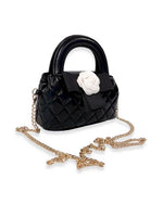 Small black quilted handbag with rounded top handles, decorated with a large white flower and black bow, featuring a gold-tone chain shoulder strap.
