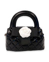 Small black quilted handbag with rounded handles, featuring a large black ribbon and a white fabric flower embellishment on the front.
