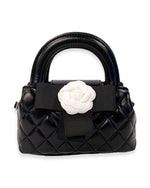Small black quilted handbag with rounded handles, featuring a large black ribbon and a white fabric flower embellishment on the front.