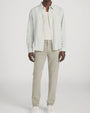 Person standing in a studio against a light neutral background, wearing a light striped button-down shirt with long sleeves left open over a cream ribbed tank top. The outfit is paired with slim-fit khaki pants and white lace-up sneakers, photographed in a full-length, front-facing pose.