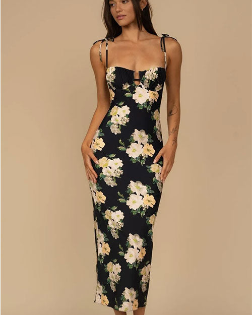 Person wearing a fitted, sleeveless black dress with thin tie straps and a large floral print featuring white and light yellow flowers with green leaves.