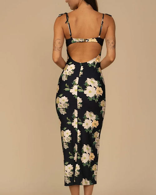 Back view of a fitted, sleeveless black dress with thin tie straps, a large white and light yellow floral print, and an open back cutout detail.