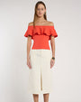 Close-up studio image against a light neutral background, showing an off-the-shoulder coral top with a wide, layered ruffle neckline. 