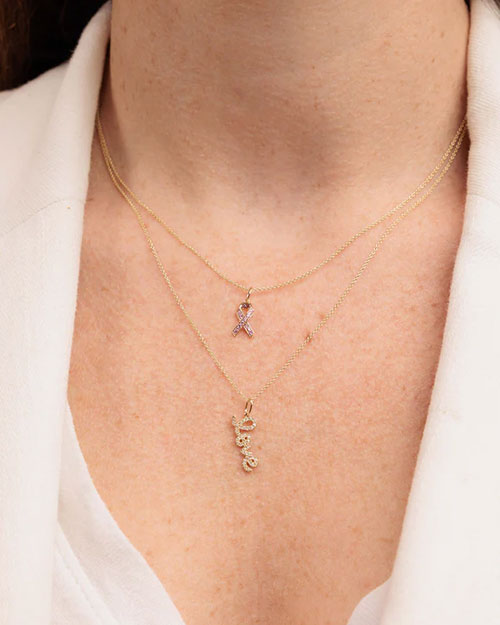 Two layered gold necklaces. The shorter necklace features a ribbon-shaped pendant, and the longer necklace has a cursive “love” pendant.