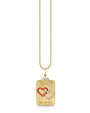 Gold necklace with a rectangular pendant featuring two interlocking hearts—one outlined in red gemstones and the other in white—along with two small fish-like symbols above. The bottom of the pendant is engraved with “THE LOVERS.”