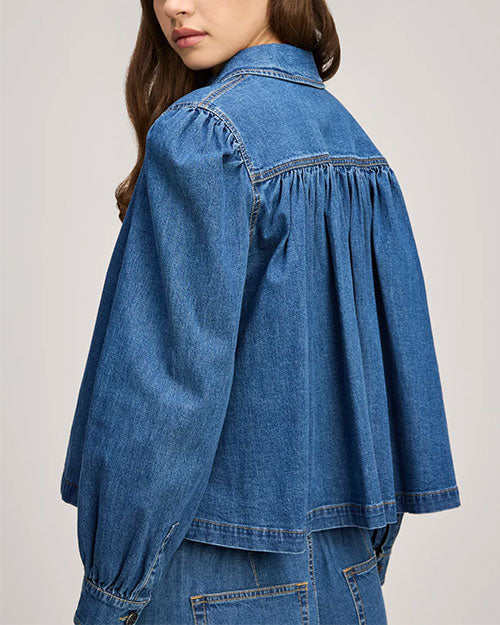 Back view of a blue denim top with gathered yoke detail, long sleeves, and a loose, flowy silhouette.