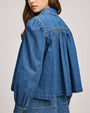 Back view of a blue denim top with gathered yoke detail, long sleeves, and a loose, flowy silhouette.