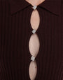 Close-up of a ribbed dark burgundy knit fabric featuring three oval cutouts down the center, each connected by a square silver rhinestone clasp. The top of the garment has a pointed collar.