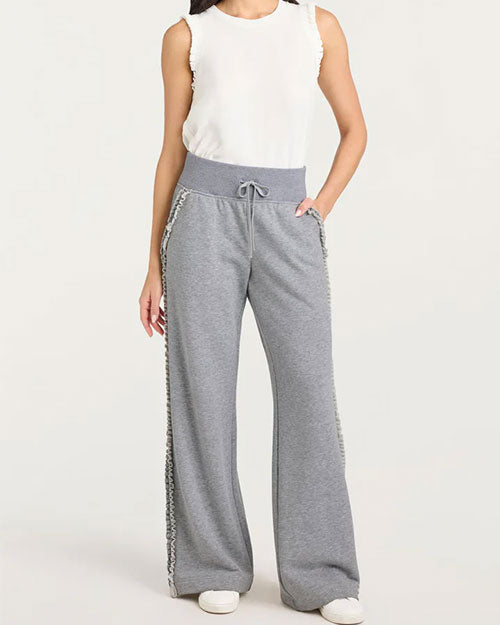 A pair of gray wide-leg sweatpants with a high ribbed waistband and drawstring tie. The pants feature ruffled trim running down the outer side seams for added detail. They are styled with a sleeveless white top and white sneakers, creating a casual and comfortable look.