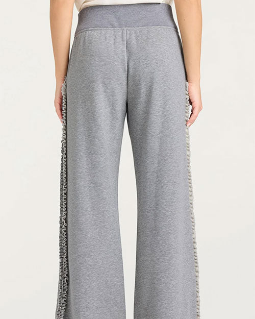 Back view of a person wearing gray wide-leg pants with a high ribbed waistband and ruffled trim running down the outer sides of both legs.