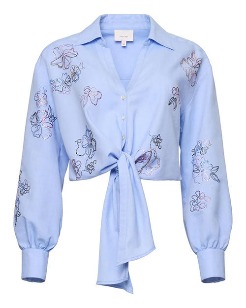 Front view of a light blue cropped button-down blouse featuring delicate embroidered floral motifs, a pointed collar, long sleeves with gathered cuffs, and a tie-front hem, displayed against a white background.