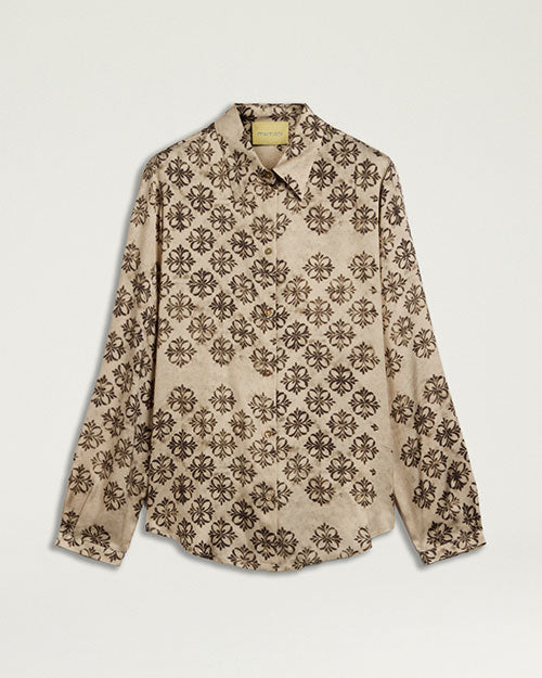 Product image of a cream-colored long-sleeve blouse featuring an allover black floral-inspired print. The blouse has a pointed collar, button-front closure, buttoned cuffs, and a relaxed fit with a gently curved hem. Shown laid flat against a light gray background.