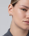 Close-up of a person wearing a small, chunky two-tone hoop earring featuring interlocking gold and silver bands with a polished finish.