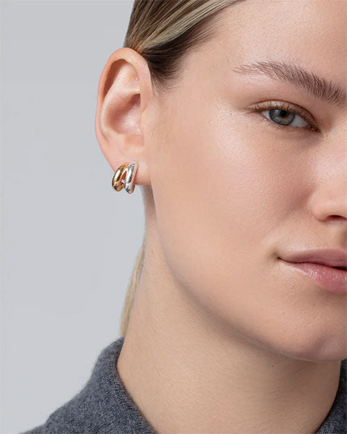 Close-up of a person wearing a small, chunky two-tone hoop earring featuring interlocking gold and silver bands with a polished finish.