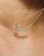 Close-up of a gold necklace with two chains. One chain features a pendant spelling “mom” in cursive letters adorned with sparkling stones, along with a small bee-shaped charm.