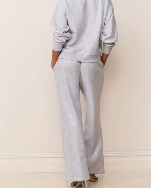 Back view of a light blue loungewear set featuring a relaxed-fit sweatshirt and wide-leg pants with a subtle tonal floral pattern. The outfit is paired with metallic strappy high-heeled sandals.
