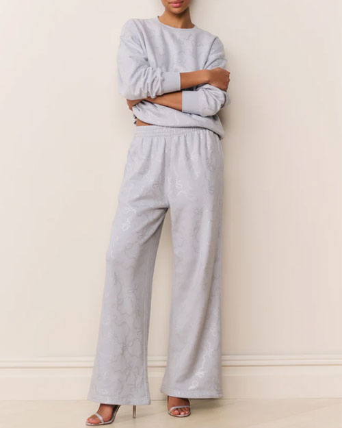 Light blue two-piece loungewear set featuring a relaxed-fit long-sleeve sweatshirt and wide-leg pants with a subtle tonal floral pattern. The outfit is paired with strappy high-heeled sandals.