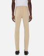 Back view of a person standing in a studio against a light neutral background, wearing a white sleeveless top tucked into slim-fit khaki pants. The pants feature a mid-rise waist, belt loops, a button and zip closure, and classic five-pocket styling. The look is paired with black leather shoes, photographed in a full-length, front-facing pose.