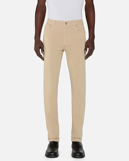 Person standing in a studio against a light neutral background, wearing a white sleeveless top tucked into slim-fit khaki pants. The pants feature a mid-rise waist, belt loops, a button and zip closure, and classic five-pocket styling. The look is paired with black leather shoes, photographed in a full-length, front-facing pose.