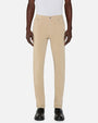 Person standing in a studio against a light neutral background, wearing a white sleeveless top tucked into slim-fit khaki pants. The pants feature a mid-rise waist, belt loops, a button and zip closure, and classic five-pocket styling. The look is paired with black leather shoes, photographed in a full-length, front-facing pose.