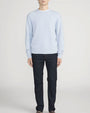 Person standing in a studio against a light neutral background, wearing a light blue crewneck sweater with ribbed neckline, cuffs, and hem, paired with dark-wash straight-leg jeans. The image is photographed in a full-length, front-facing pose.