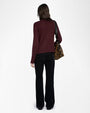  Back view of an outfit featuring a dark burgundy knit turtleneck sweater paired with black high-waisted pants. The person is carrying a leopard-print shoulder bag with a black strap. The sweater has a ribbed hem and cuffs, and the pants have a straight-leg fit.