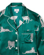 Green satin pajama top with a white leopard print pattern, featuring a collar, white piping along the edges and cuffs, a button-down front, and a left chest pocket with piping detail. The label inside reads "Petite Plume."