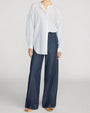 Blue and white striped oversized button-front shirt with a split neckline, paired with dark wash wide-leg jeans.