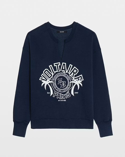 A navy blue long‑sleeve sweatshirt featuring a split crew neckline and a large printed graphic on the front. The design includes the text “VOLTAIRE PARIS” in bold white letters arranged in an arc, a circular emblem with additional lettering, two stylized palm trees, and small text reading “Est. 1997” and “art is truth.” The sweatshirt has a relaxed fit and a ribbed hem and cuffs.