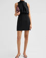 
Black sleeveless mini dress with a gathered high neckline, fitted skirt, burgundy clutch, and black heeled sandals.