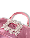 Close-up of a metallic pink handbag with a top handle, featuring a large rectangular crystal embellishment made of clear, faceted stones on the front flap.