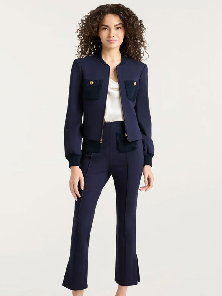 Navy tailored pantsuit with a cropped jacket featuring gold buttons and contrasting textured pockets, worn over a light satin top.
