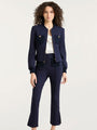 Navy tailored pantsuit with a cropped jacket featuring gold buttons and contrasting textured pockets, worn over a light satin top.