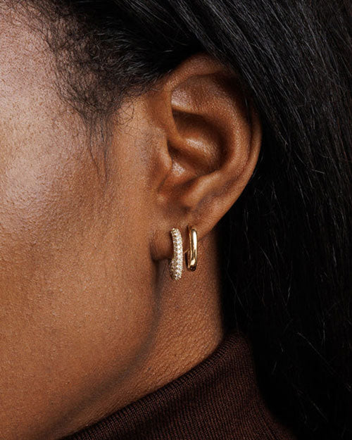 Close-up of an ear wearing two small hoop earrings: one plain gold and the other decorated with small, sparkling stones.